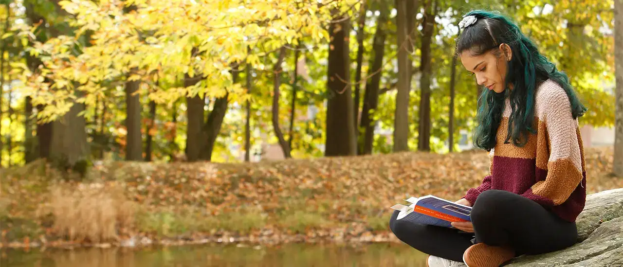 Person reading on a rock next to SUNY Oneonta's Hunt Union Pond