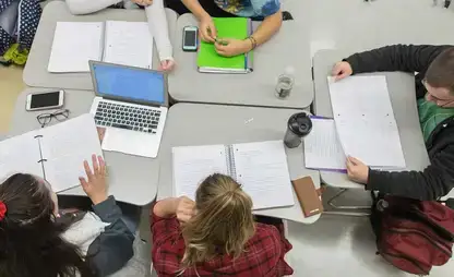view from above of people working at a workspace covered in notebooks, binders and a laptop
