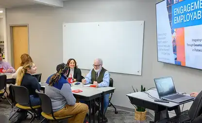 modern workspace with people sitting at tables and a presenter working at a laptop and large display